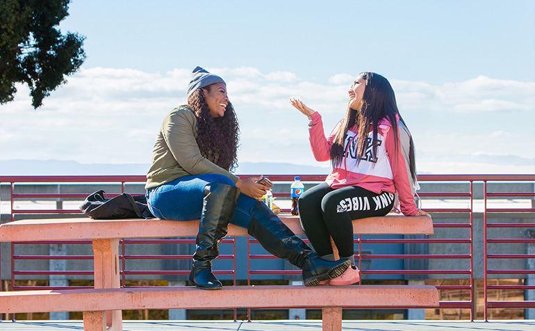 Two female students sitting on a lunch table and chatting