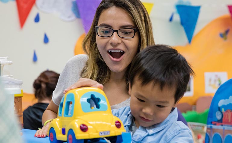 Woman holds small child playing with toy bus