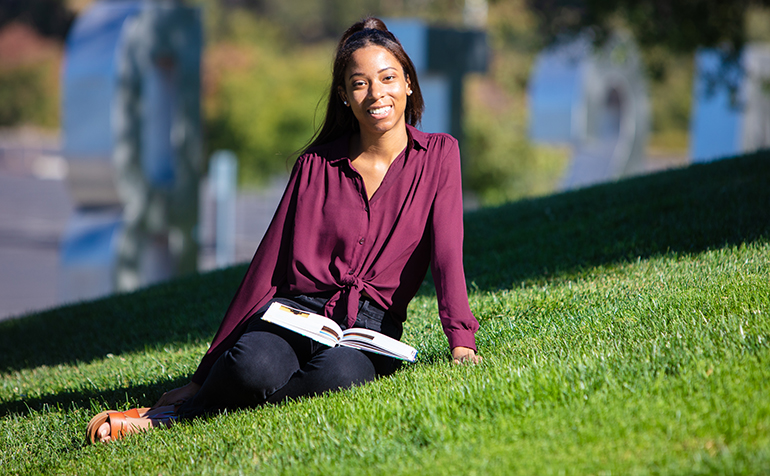 Female student smiling sits in grass