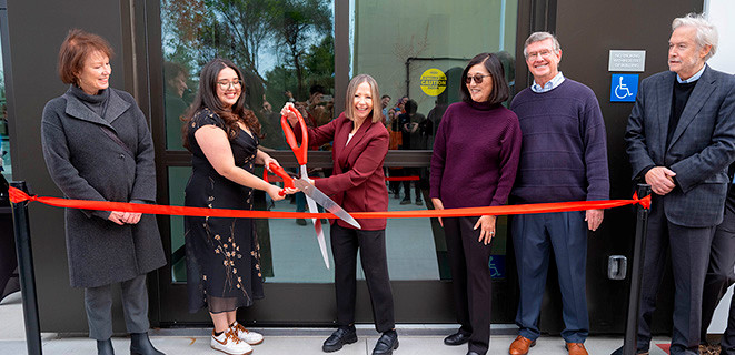 President Cathy Sandeen and campus partners cutting the red ribbon in front of the Braddock Center