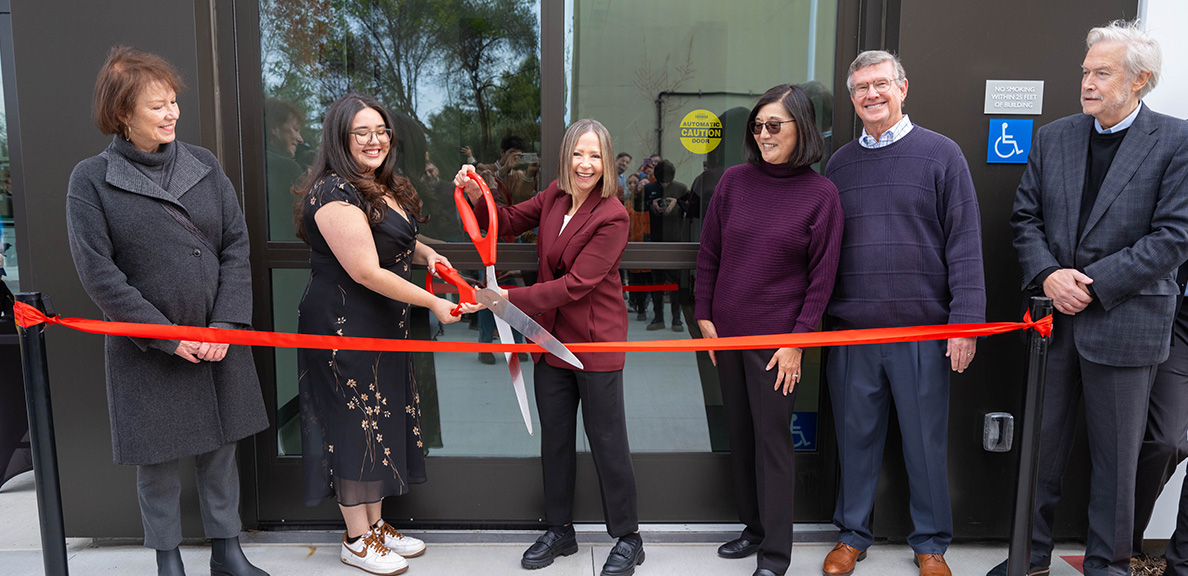 President Cathy Sandeen and campus partners cutting the red ribbon in front of the Braddock Center